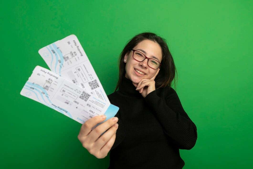 A person in a black sweater holds three travel tickets against a bright green background.
