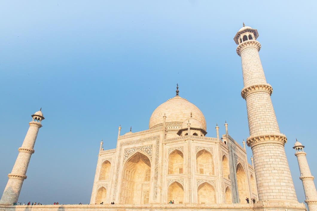 The Taj Mahal, a white marble mausoleum, towers majestically against a clear blue sky, showcasing its intricate architecture.